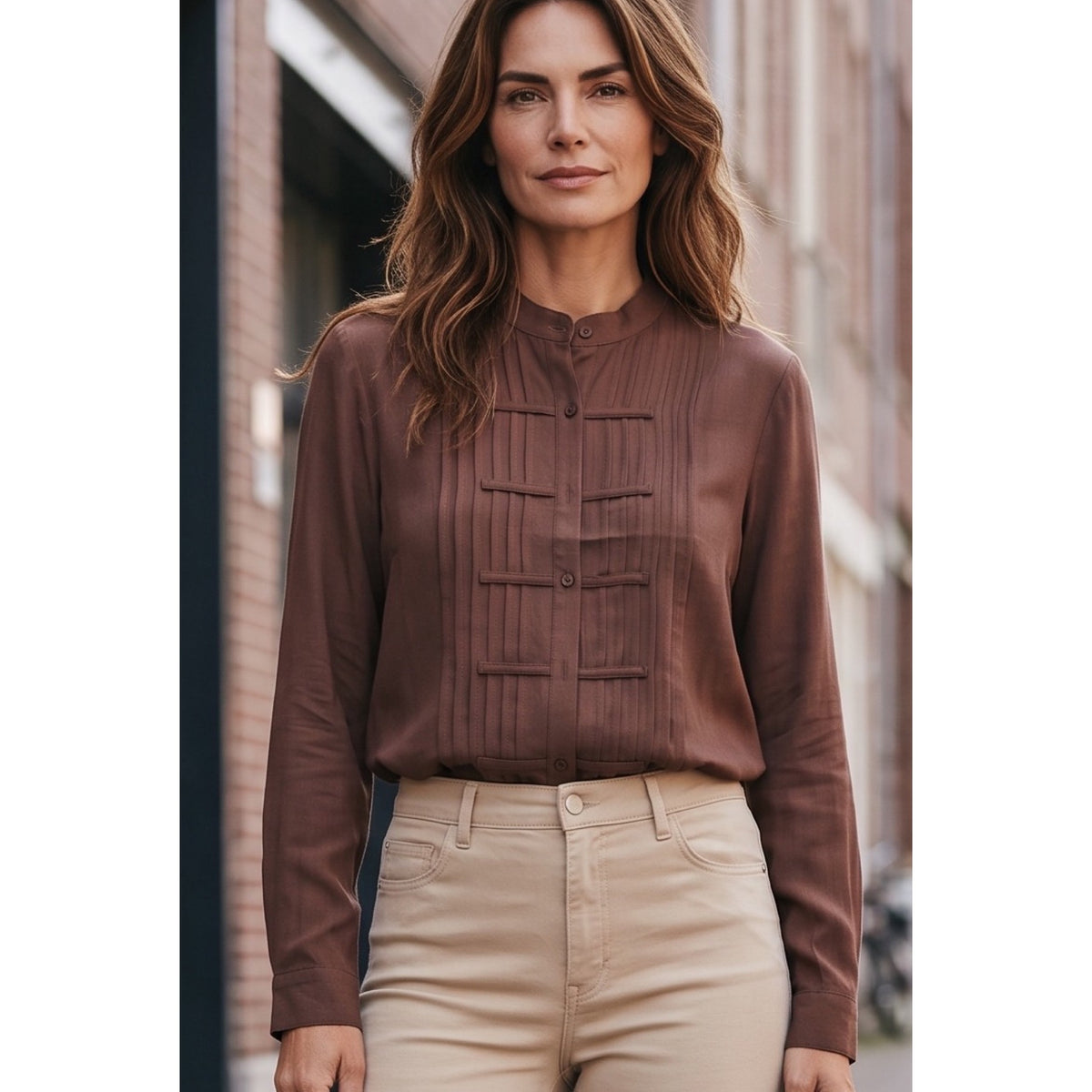 Vista cercana de la blusa marrón con cuello mao, botones al tono y detalles decorativos en el delantero.