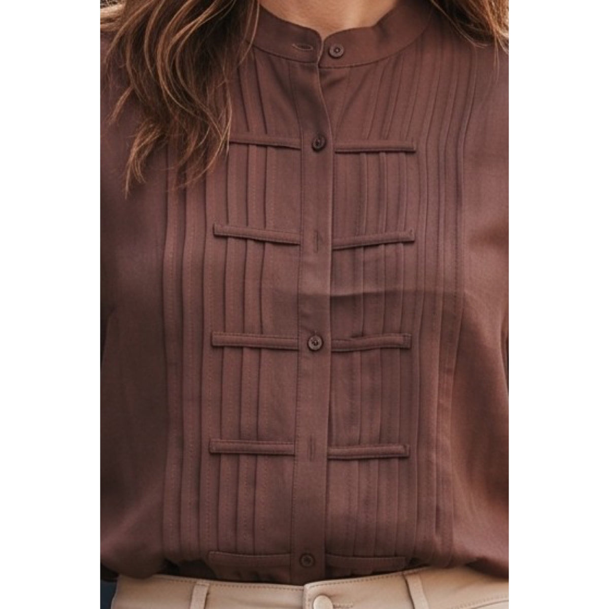 Detalle de las alforzas verticales, las tiras horizontales y los botones de la blusa marrón.