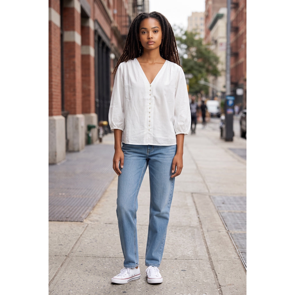 Modelo con blusa blanca de escote en pico y mangas tres cuartos, combinada con vaqueros y zapatillas blancas.