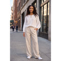 Modelo con blusa blanca de bordado inglés y lazada, llevada parcialmente por dentro de un pantalón beige.