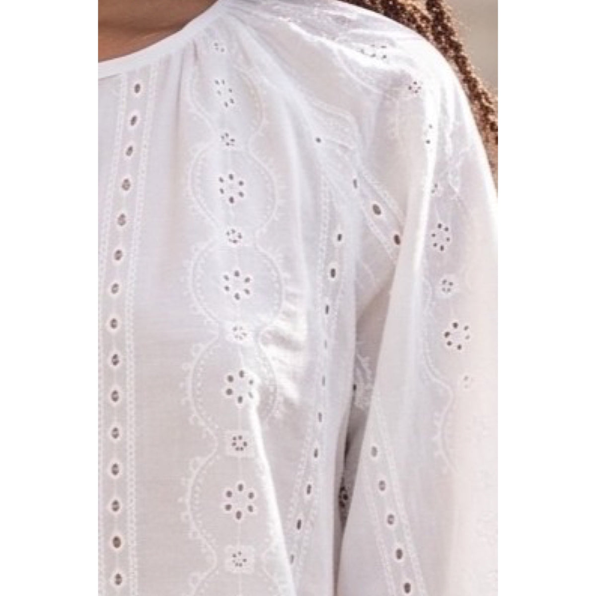 Detalle del bordado inglés con motivos florales y franjas verticales caladas en la blusa blanca.