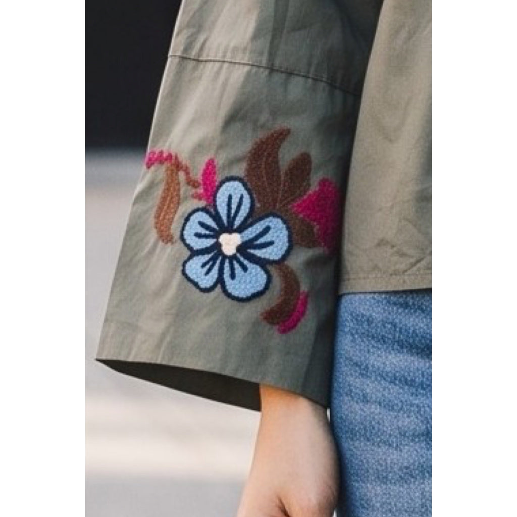 Detalle del bordado floral azul, marrón y fucsia en la manga acampanada de una camisa caqui.