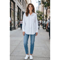 Modelo con camisa blanca larga de cuello clásico y bajo redondeado, combinada con vaqueros y zapatillas blancas.