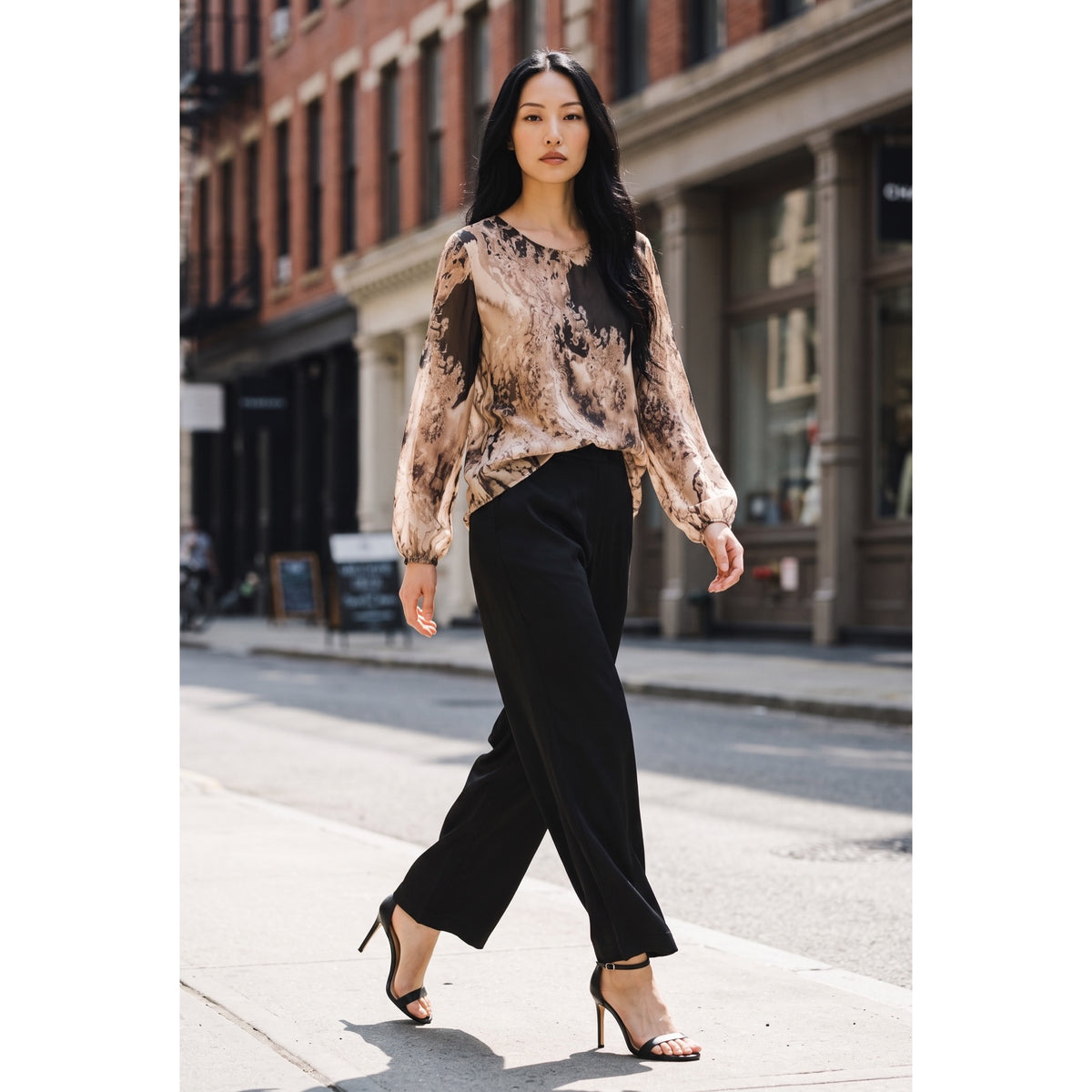Modelo con conjunto de seda formado por blusa de estampado marmoleado en beige y tonos oscuros y pantalón palazzo negro.