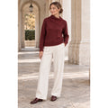 Modelo con jersey burdeos de cuello asimétrico plegado y manga larga, combinado con pantalón crudo.
