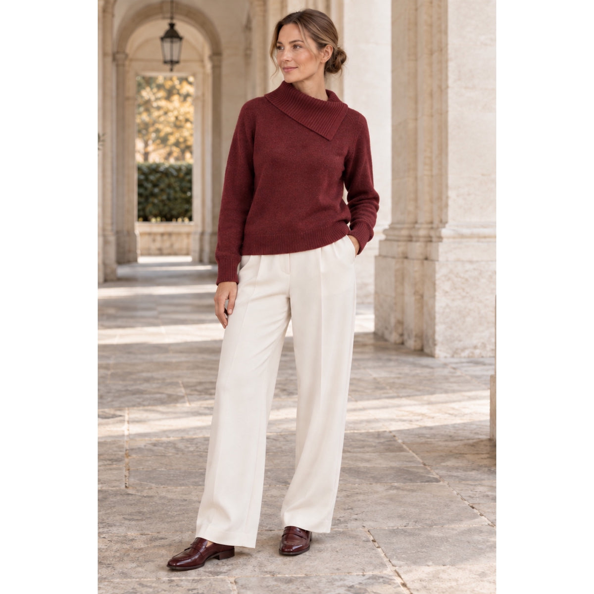 Modelo con jersey burdeos de cuello asimétrico plegado y manga larga, combinado con pantalón crudo.