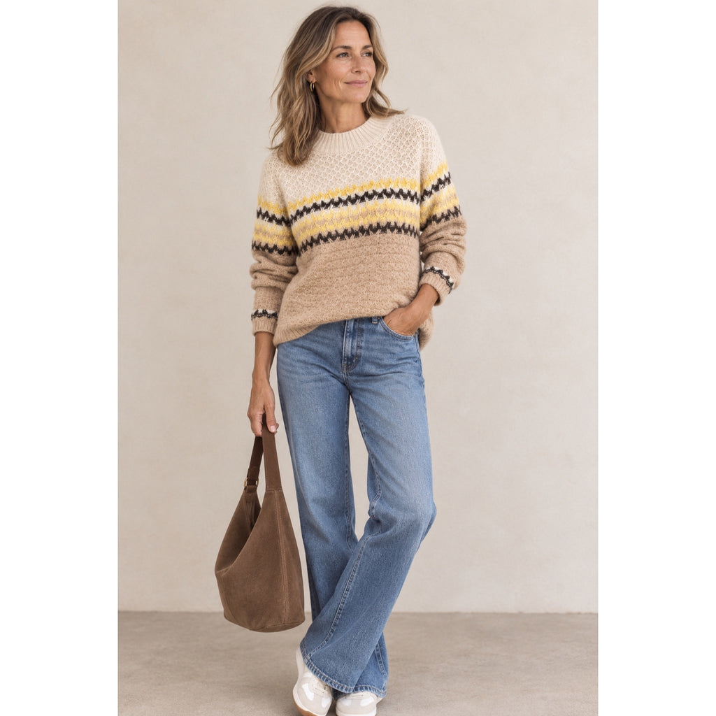 Modelo con jersey camel y crudo con franjas amarillas y oscuras, combinado con vaqueros y bolso marrón.