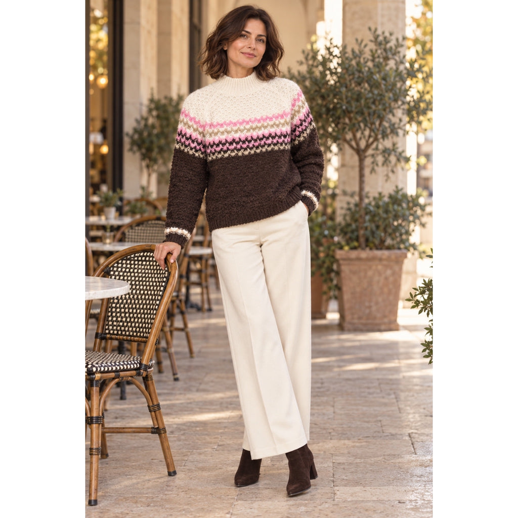 Modelo con jersey choco y crudo con franjas geométricas rosas y beige, combinado con pantalón marfil.