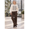 Modelo con jersey marfil de cuello redondo, cordones oscuros y perlas decorativas, combinado con pantalón marrón.