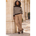 Modelo con jersey de cuello alto marrón chocolate y rayas beige, combinado con pantalón camel.