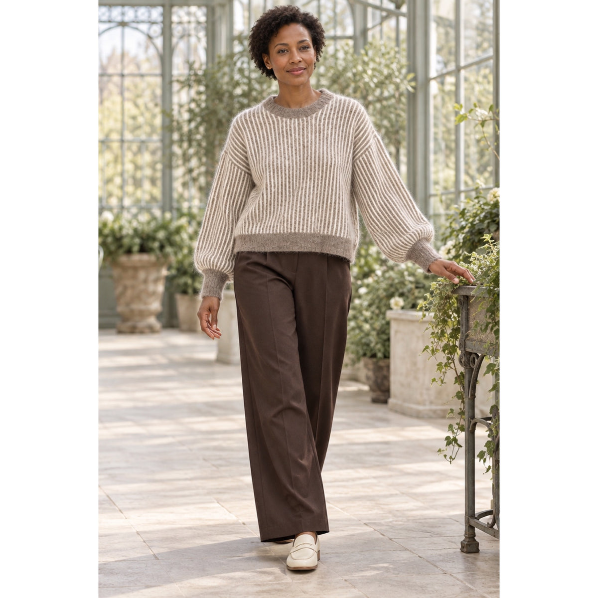 Modelo con jersey taupe y crudo de rayas verticales, cuello redondo y mangas abullonadas, combinado con pantalón marrón.