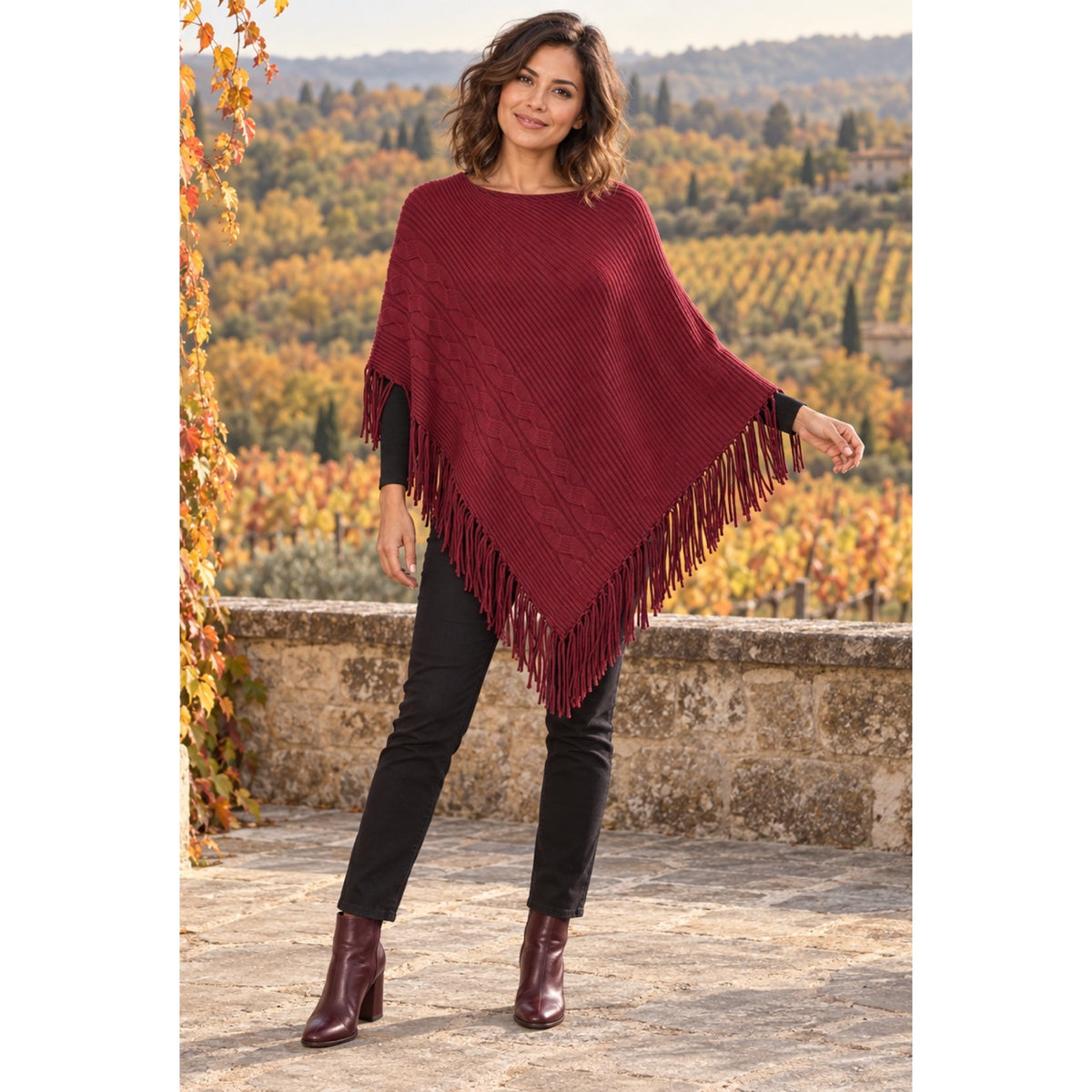 Modelo con poncho de punto acanalado, trenzas en relieve y flecos largos, combinado con pantalón negro.